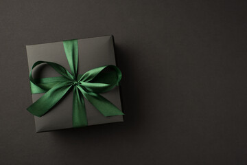 Top view photo of black giftbox with green ribbon bow on isolated black background with empty space