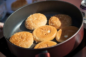 Sesame buns for burgers are lying in a frying pan.