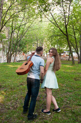 Fototapeta premium A young couple a man and a girl with a guitar walk in the park in the summer