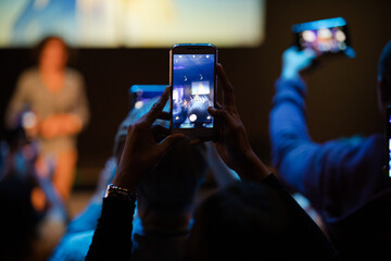 Audience members with smart phones videoing speaker on stage at conference