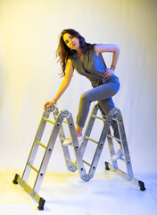 girl beautifully posing on a stepladder. full length portrait. interesting posing with construction tools