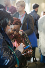 Smiling businesswomen using smart phone in conference audience