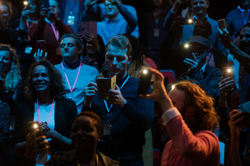 Fototapeta na wymiar Smiling audience using smart phone flashlights for speaker