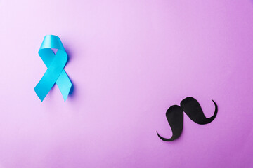 Black mustache paper and light blue ribbon, studio shot isolated on purple background, Prostate cancer awareness month, Fathers day, minimal November moustache concept