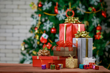 Colorful small and big present gift boxes with shiny ribbon bow tie placed on corner of wooden table in front fully decorative beautiful Christmas eve pine tree and brick wall in blurred background