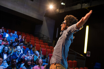 Audience watching male speaker with arms outstretched on stage