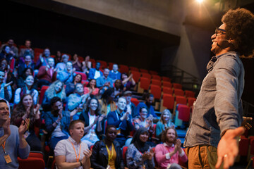 Audience watching male speaker with arms outstretched on stage