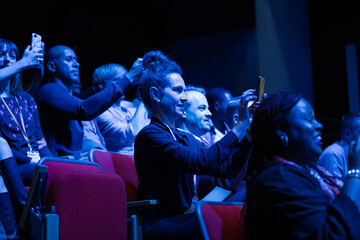 Fototapeta na wymiar Audience members with smart phones videoing speaker on stage at conference