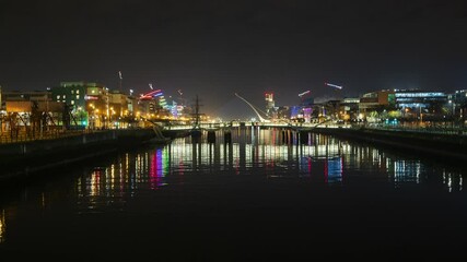 Time lapse of nighttime road traffic and people walking by over Liffey river reflecting lights in the distance in Dublin City Centre in Ireland.