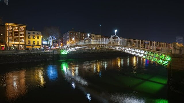 Time lapse of nighttime road traffic and people walking over the historical bridge on Liffey river in Dublin City Centre in Ireland.