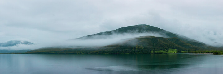 Misty Lake As Fog Rolls Against A Green Mountain Background
