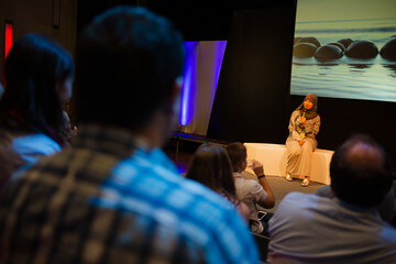 Smiling female speaker in hijab talking with microphone on stage