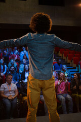 Audience watching male speaker with arms outstretched on stage