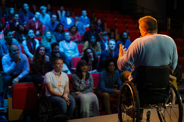 Obraz premium Speaker in wheelchair on stage talking to conference audience