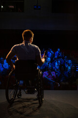 Fototapeta na wymiar Female speaker in wheelchair on stage talking to audience