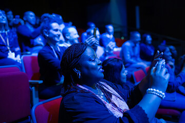 Audience members with smart phones videoing speaker on stage at conference