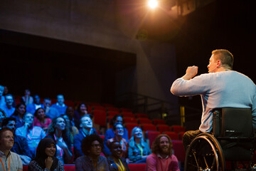 Speaker in wheelchair on stage talking to conference audience