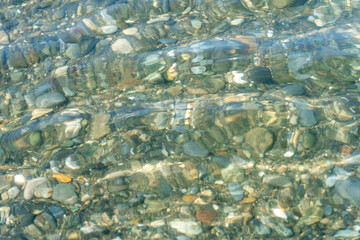 Background of wet pebbles on the bottom of the sea, which is washed by a sea wave