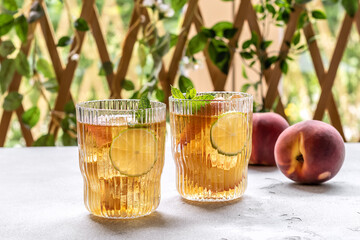 Two glasses with homemade peach ice tea or lemonade with mint. Summer cold drink with ripe fruits and ice. . Non-alcoholic cocktail or kombucha drink.