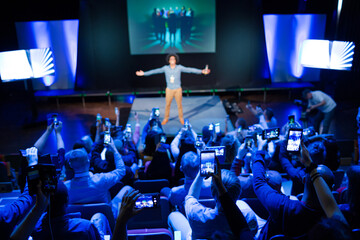 Audience members with smart phones videoing speaker on stage at conference