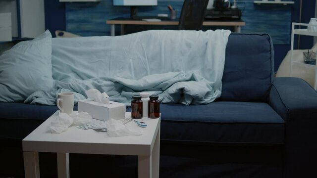 Nobody in living room with medical treatment against flu and seasonal cold. Close up of table with medicaments, medicine, vitamins, bottles of pills, thermometer and cup of tea.