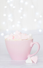 Pink cup with marshmallows in the shape of hearts on a background of lights. Image with selective focus