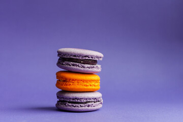 Multicolored macarons on a purple background. French dessert for Halloween. Almond flour baked goods.