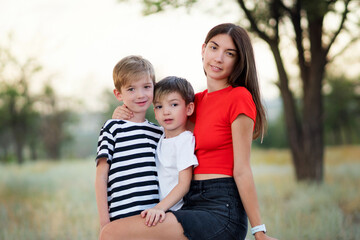 Fototapeta premium Happy young family having fun outdoors. Young family mother and two little sons playing together in rural settings in summer day. Mom and children hugging.