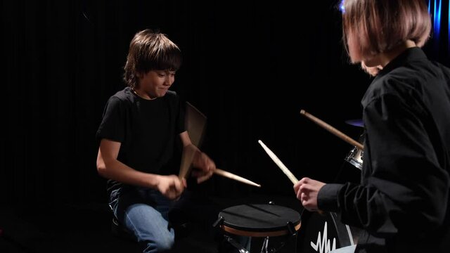 Young caucasian woman teaches a boy to play the drums in the studio on a black background. Music school student