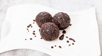 Chocolate muffins on a white plate. Sprinkled with chocolate and coconut on top. Homemade fluffy and juicy chocolate cakes. On a gray background