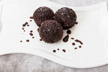 Chocolate muffins on a white plate. Sprinkled with chocolate and coconut on top. Homemade fluffy and juicy chocolate cakes. On a gray background