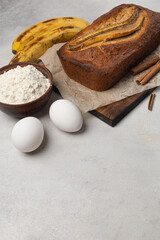 Fototapeta na wymiar Ready fresh banana bread in a rectangular baking dish with ingredients on a light background