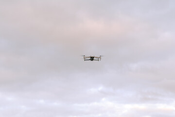 Fototapeta na wymiar Quadcopter drone hovering in the air with clouds in background