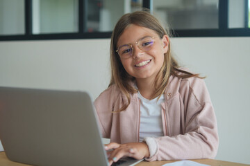 Naklejka premium young girl with glasses working on laptop doing her lessons at home