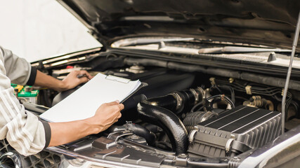 Automobile mechanic repairman checking a car engine with inspecting writing to the clipboard the...
