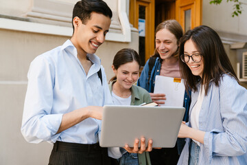 Multiracial students using laptop and laughing while standing outdoors