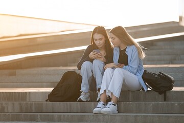 Two teenage students girls at the building of university using smartphone, back to school 