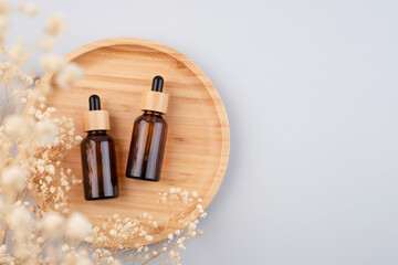 Amber glass dropper bottles different sizes with bamboo lid on wooden podium for product presentation. Top view on grey background with dry plants. Skincare product . Beauty concept for face body care