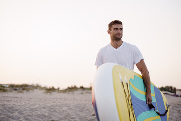 Fototapeta premium Young man carrying sup board after water surf session
