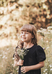 Little girl in a black stylish dress in nature in the summer with flowers
