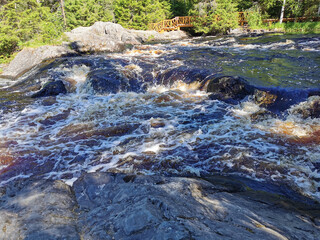 Naklejka na ściany i meble View of the bubbling waterfall with brown water on the Tokhmayoki River in Karelia from the ecological trail