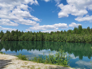 The shore of the lake Light with turquoise water, which reflects the trees and the sky with clouds, in the mountain park Ruskeala.