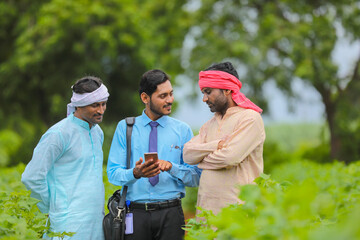 Young indian agronomist or banker showing some information to farmer in smartphone at agriculture...