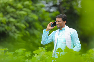 Indian farmer talking on smartphone at green agriculture field