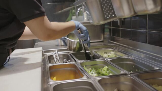 Fast food worker tossing salad in bowl