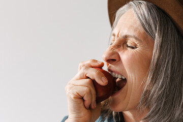 Grey senior woman in hat eating apple with her eyes closed