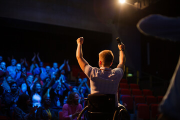 Fototapeta na wymiar Female speaker in wheelchair on stage waving to audience
