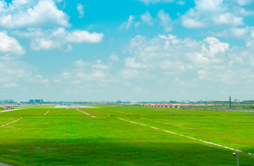 Landscape of the airport runway and green grass field with blue sky and white clouds. Plane on taxiway. Airplane take off at taxiway of the airport. Aviation business. Cityscape aroud the airport.