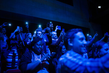 Eager audience with smart phone flashlights in dark auditorium