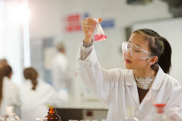 Girl student examining pink liquid, conducting scientific experiment in laboratory classroom - obrazy, fototapety, plakaty